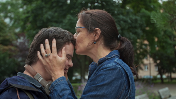 A happy mature mother kissing on forehead her adult son with Down syndrome outdoors in town.