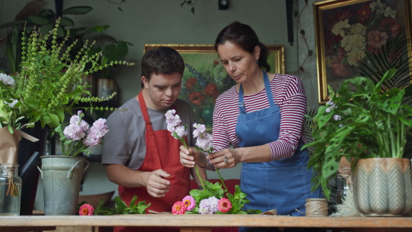 A young male florist with Down syndrome working with help of mentoring colleague indoors in flower shop