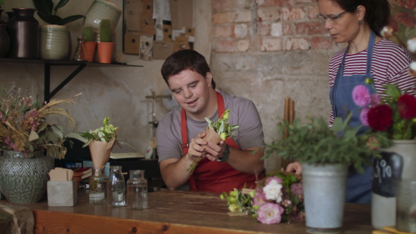 A young male florist with Down syndrome working with help of mentoring colleague indoors in flower shop