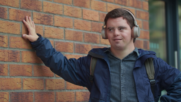 A happy young man with Down syndrome with headphones listening to music outdoors.