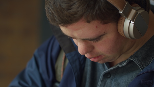 A close up of man with Down with headphones using smartphone outdoors.