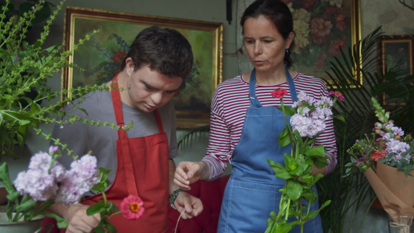 A young male florist with Down syndrome working with help of mentoring colleague indoors in flower shop