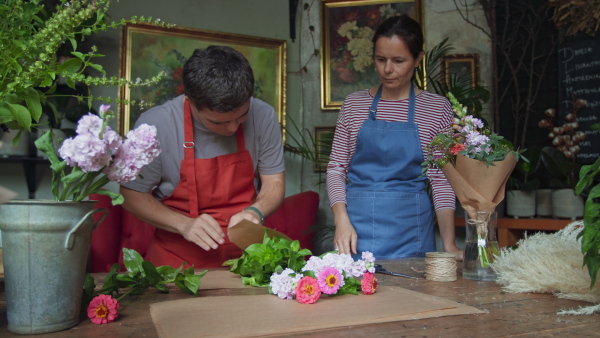 A young male florist with Down syndrome working with help of mentoring colleague indoors in flower shop