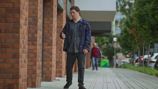 A low angle view of Down syndrome man walking outdoors in town street.