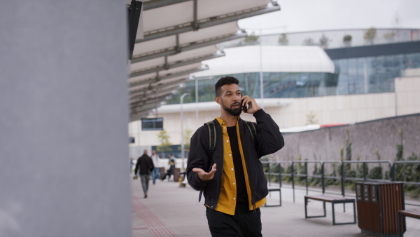 A young African- american man commuter walking in bus station and using smartphone.