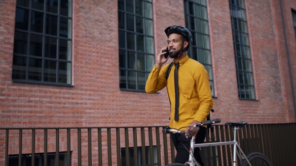 A young man commuter pushing bike and using smartphone in city.