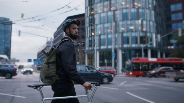 A young African-american man commuter with bicycle crossing the road in city.