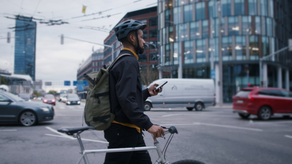 A young African-american man commuter with bicycle crossing the road in city.