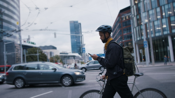 A young African-american man commuter with bicycle crossing the road in city.