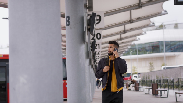 A young African- american man commuter walking in bus station and using smartphone.