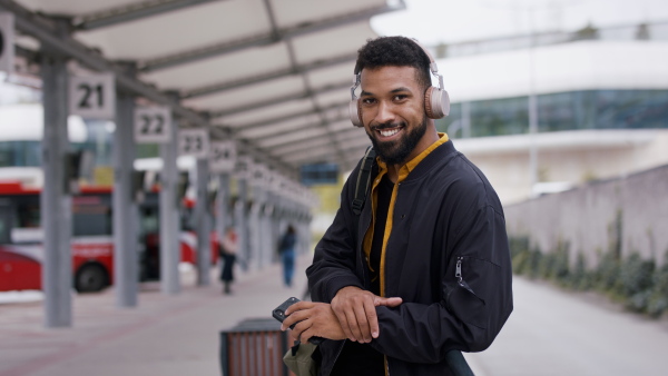 A young African- american man commuter using smartphone and looking at camera at bus station.