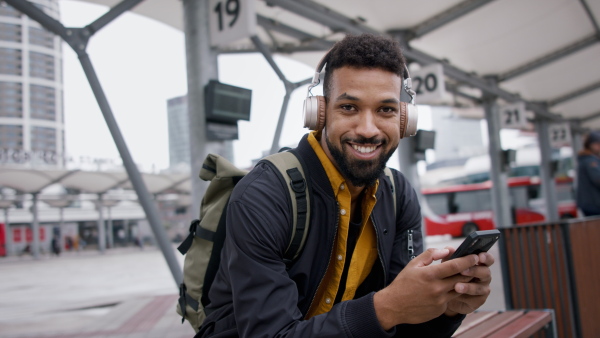 A young African- american man commuter using smartphone and looking at camera at bus station.