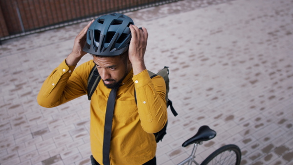 A high angle view of young man commuter with bike putting on cycling helmet.