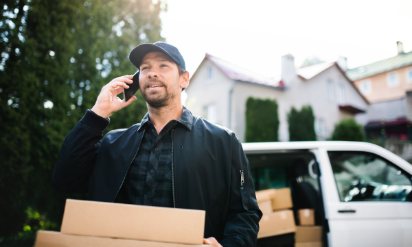 Delivery man courier delivering parcel box outdoors in town using smartphone.