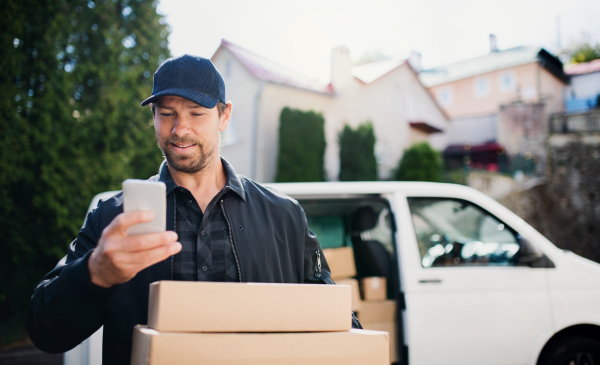 Delivery man courier delivering parcel box outdoors in town using smartphone.