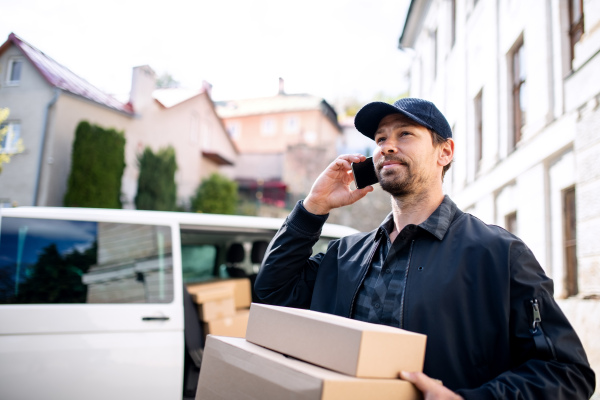 Delivery man courier delivering parcel box outdoors in town using smartphone.