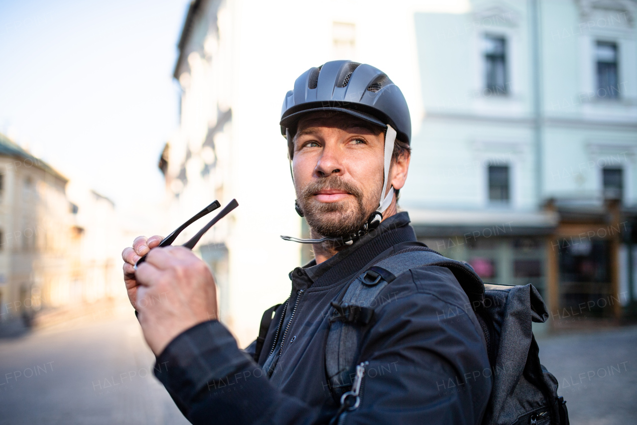 Delivery man courier with bicycle helmet and sunglasses standing in town.