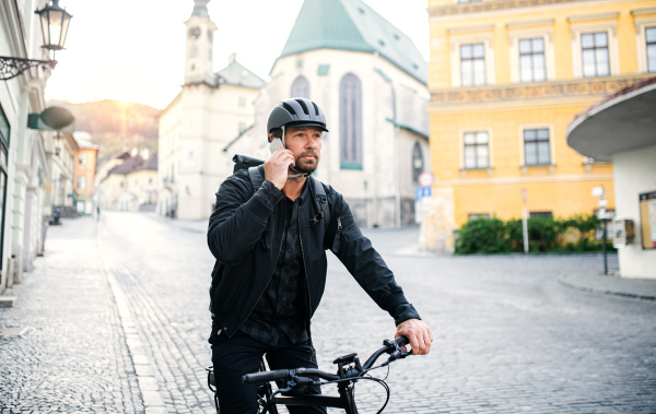 Front view portrait of delivery man courier with bicycle in town, using smartphone.