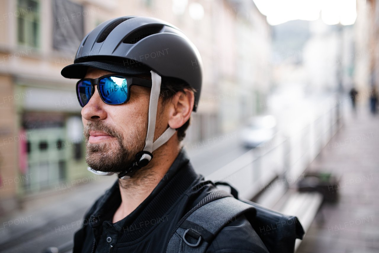 Delivery man courier with bicycle helmet and sunglasses standing in town.