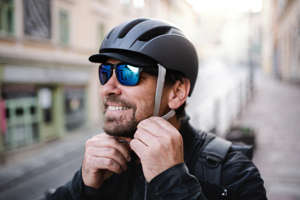 Delivery man courier fastening bicycle helmet and sunglasses standing in town.