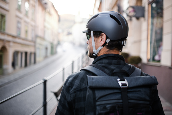 Rear view of delivery man courier with backpack and bicycle helmet walking in town.