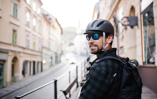 Delivery man courier with bicycle helmet and sunglasses in town, looking over shoulder.