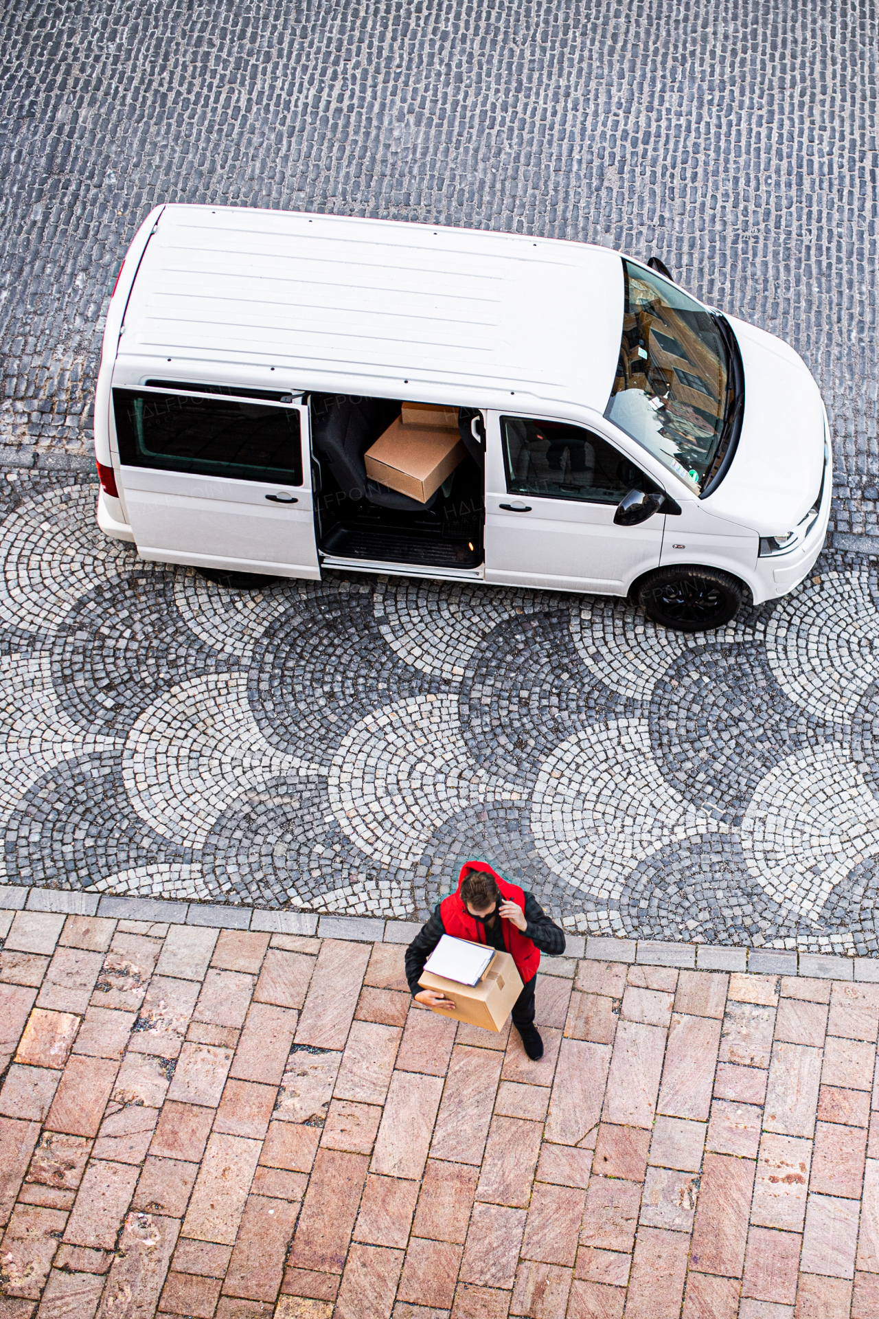 Aerial view of delivery man courier with face mask delivering parcel box in town, using smartphone.