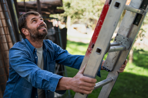 Side view of mature man climbing up at ladder.