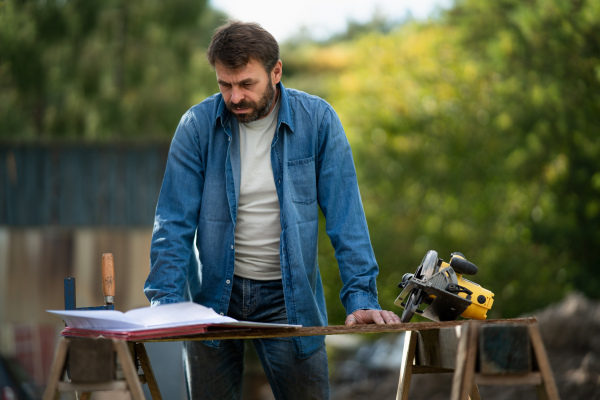 A handyman measuring a board, outside in garden.