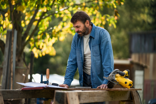 A handyman measuring a board, outside in garden.