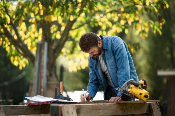 A handyman measuring a board, outside in garden.