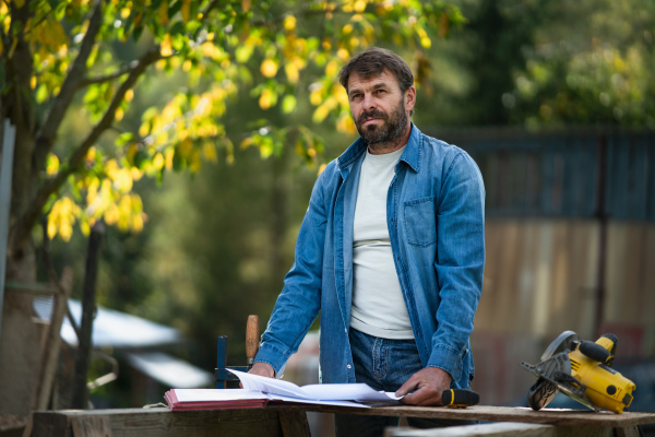 A mature man engineer with blueprints of a house outdoors.