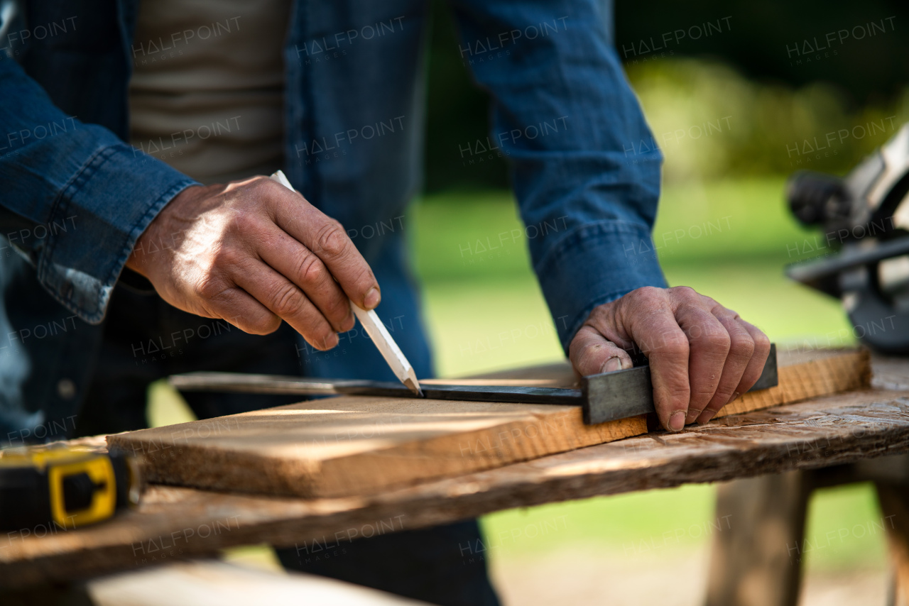 A close-up of handyman measuring a board, outside in garden.