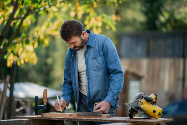 A handyman measuring a board, outside in garden.