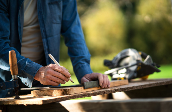 A close-up of handyman measuring a board, outside in garden.