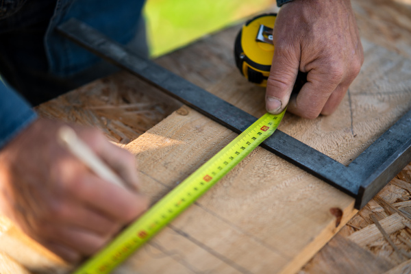 A close-up of handyman measuring a board, outside in garden.