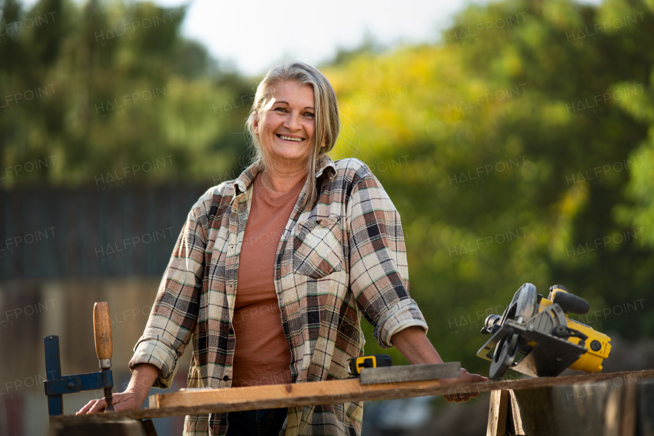 A happy handy female carpenter working in carpentry diy workshop outdoors with circular saw