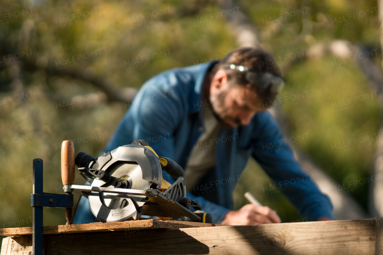 Mature handyman measuring a board, outside in garden.