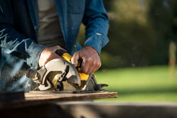 A close-up of raftsman working with circular saw at construction site