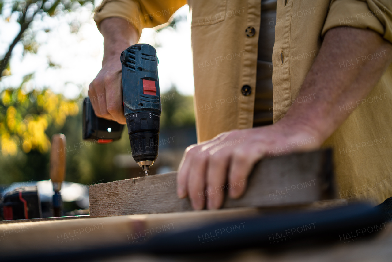 A close-up of handyman carpenter working in carpentry diy workshop outdoors with drill.