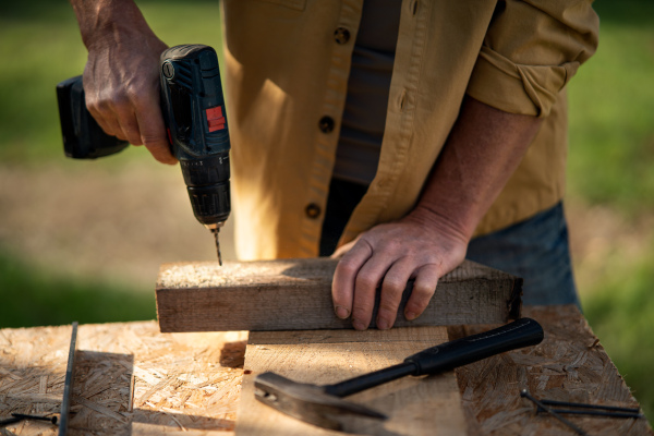 A close-up of handyman carpenter working in carpentry diy workshop outdoors with drill.