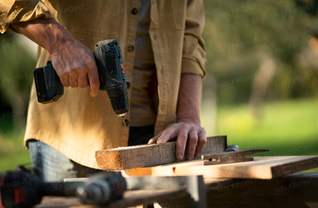 A close-up of handyman carpenter working in carpentry diy workshop outdoors with drill.