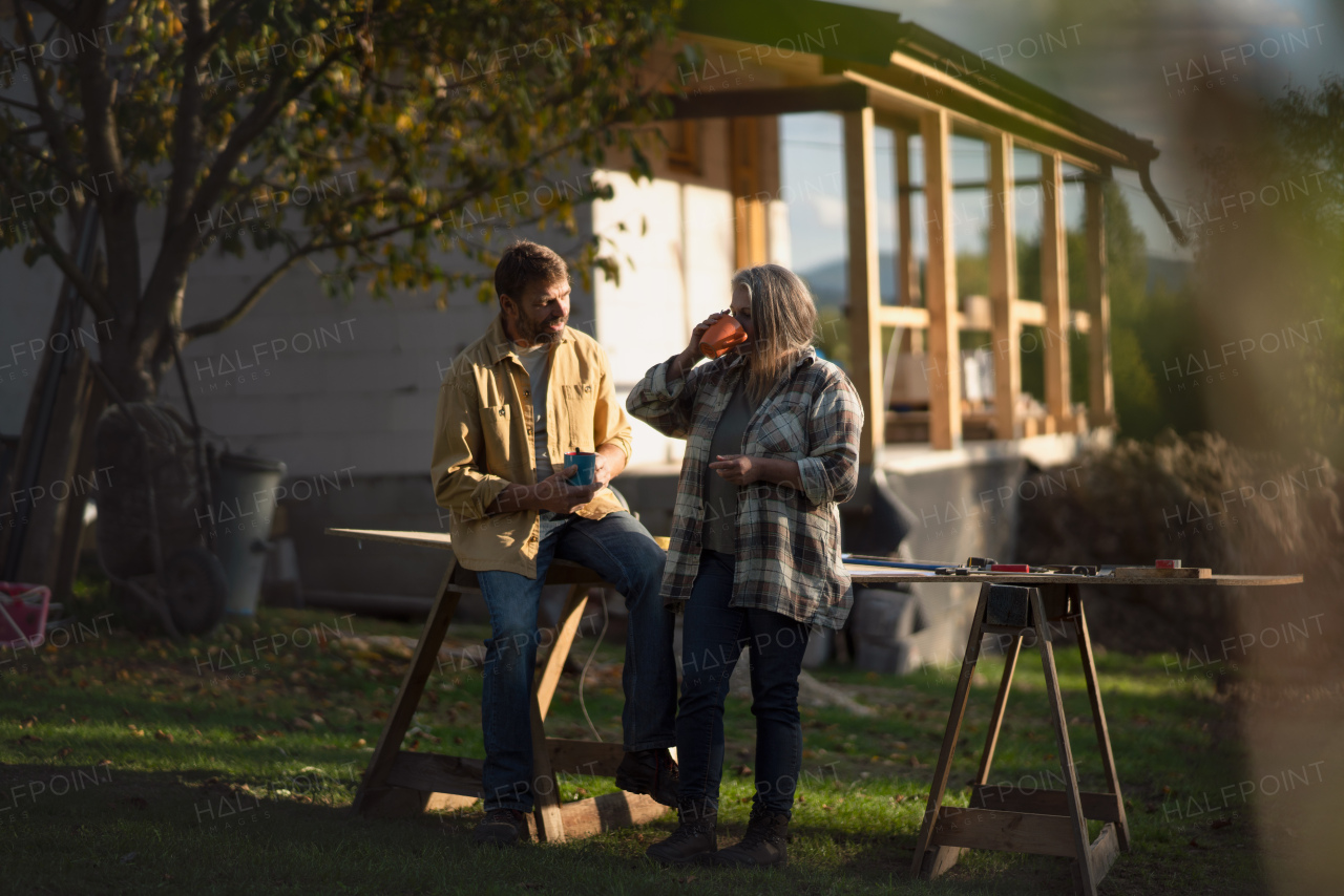 A mature couple having coffee break when working together on construction site of their new house.