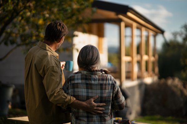 A rear view of mature couple looking at their new house under construction, planning future and dreaming.