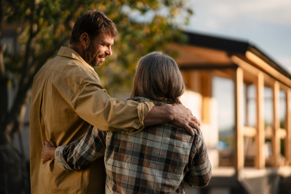 A rear view of mature couple looking at their new house under construction, planning future and dreaming.