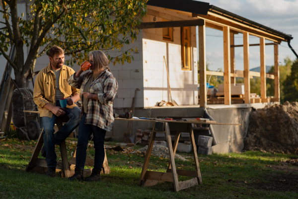 A mature couple having coffee break when working together on construction site of their new house.