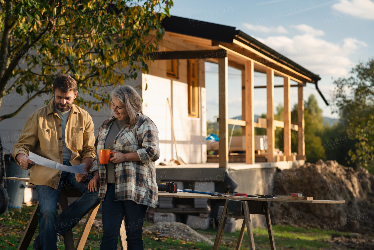 A mature couple having coffee break when working together on construction site of their new house.