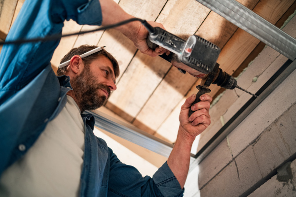 A low angle view of handyman working with drill on construction site.