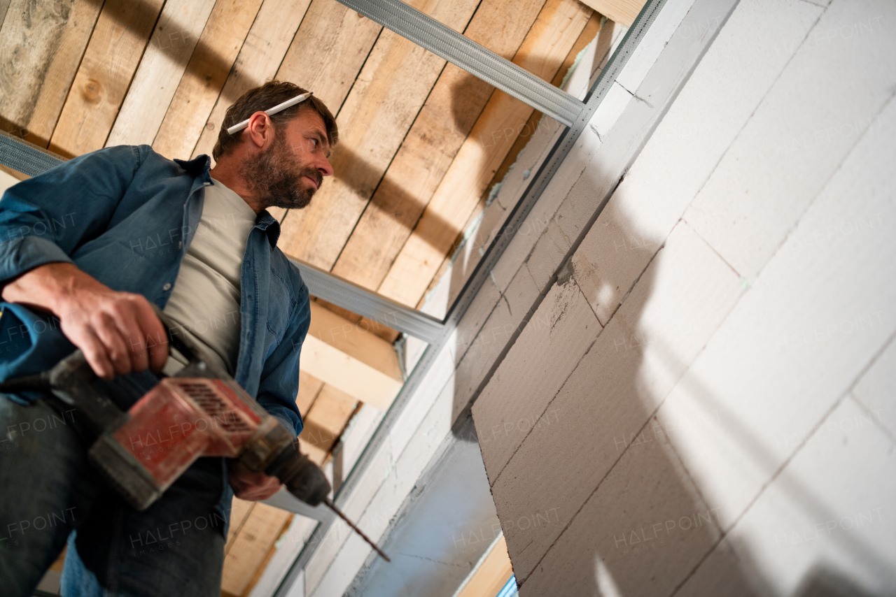 A low angle view of handyman working with drill on construction site.