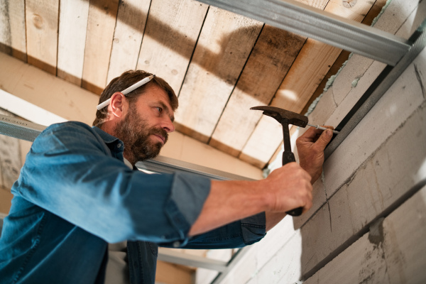 A mature handyman driving a nail in unfinished house construction, diy concept.